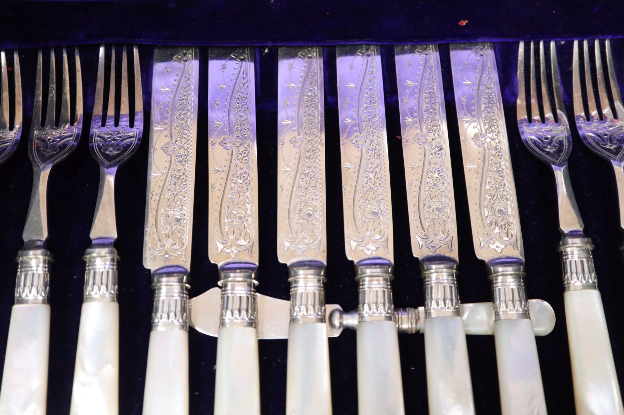 A set of twelve plated engraved mother of pearl handled dessert knives and forks, cased
